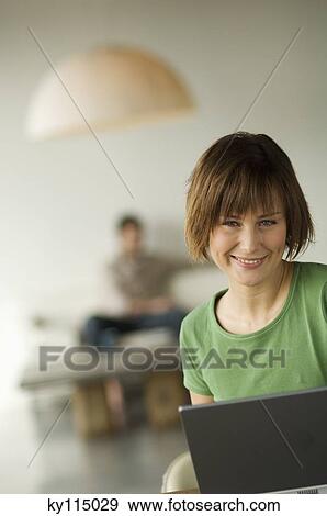 Smiling woman using laptop computer, man in the background View Large Photo Image Stock Photo - Smiling woman using laptop computer, man in the background. Fotosearch