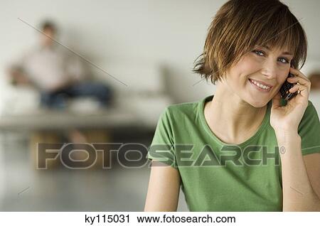 Smiling woman using mobile phone, man in the background View Large Photo Image Stock Image - Smiling woman using mobile phone, man in the background. Fotosearch