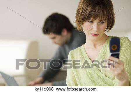 Woman using mobile phone, man using laptop computer in the background View Large Photo Image Stock Photo - Woman using mobile phone, man using laptop computer in the background. Fotosearch