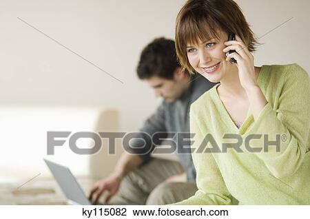 Woman using mobile phone, man with laptop computer in the background View Large Photo Image Stock Image - Woman using mobile phone, man with laptop computer in the background. Fotosearch