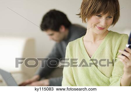 Woman using mobile phone, man with laptop computer in the background View Large Photo Image Stock Image - Woman using mobile phone, man with laptop computer in the background. Fotosearch