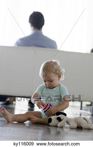 Stock Photo - Little boy with stuffed dog sitting on the floor, man in the background. Fotosearch