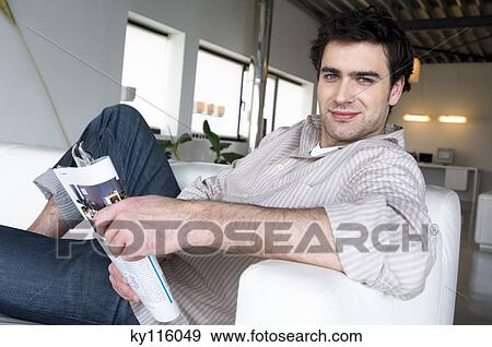 Man lying on a sofa, holding magazine, looking at the camera View Large Photo Image Stock Photo - Man lying on a sofa, holding magazine, looking at the camera. Fotosearch