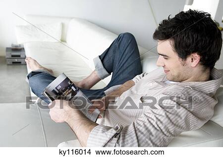 Man lying on a sofa, reading magazine View Large Photo Image Picture - Man lying on a sofa, reading magazine. Fotosearch
