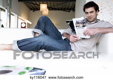Man lying on a sofa, reading magazine View Large Photo Image Stock Photo - Man lying on a sofa, reading magazine. Fotosearch