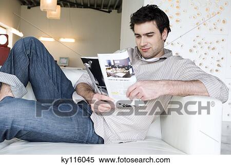 Man lying on a sofa, reading magazine View Large Photo Image Stock Photography - Man lying on a sofa, reading magazine. Fotosearch