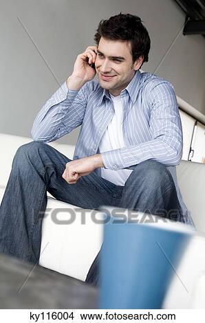 Man sitting in an armchair, using a mobile phone View Large Photo Image Picture - Man sitting in an armchair, using a mobile phone. Fotosearch