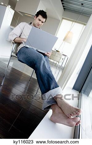 Man sitting on a chair, using laptop computer View Large Photo Image Stock Image - Man sitting on a chair, using laptop computer. Fotosearch