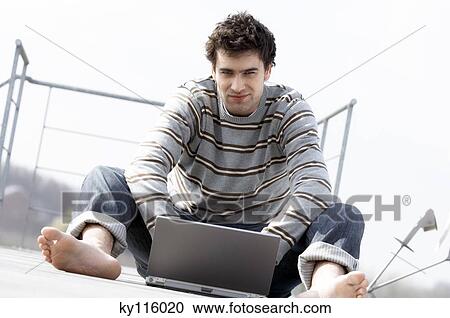 Man sitting on a terrace using laptop computer View Large Photo Image Stock Image - Man sitting on a terrace using laptop computer. Fotosearch
