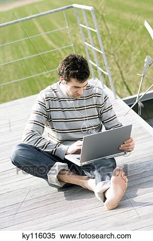 Man sitting on a terrace using laptop computer View Large Photo Image Stock Photography - Man sitting on a terrace using laptop computer. Fotosearch