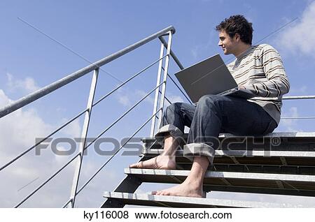 Man sitting on stairs, using laptop, outdoors, low angle View Large Photo Image Stock Photo - Man sitting on stairs, using laptop, outdoors, low angle. Fotosearch