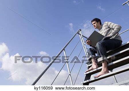 Man sitting on stairs, using laptop, outdoors, low angle View Large Photo Image Stock Photo - Man sitting on stairs, using laptop, outdoors, low angle. Fotosearch