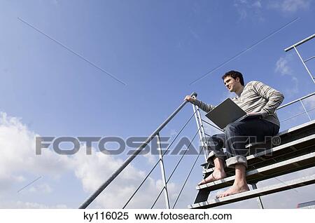 Man sitting on stairs, using laptop, outdoors, low angle View Large Photo Image Stock Photography - Man sitting on stairs, using laptop, outdoors, low angle. Fotosearch