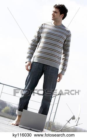 Man standing on a terrace, laptop computer on the floor View Large Photo Image Stock Image - Man standing on a terrace, laptop computer on the floor. Fotosearch