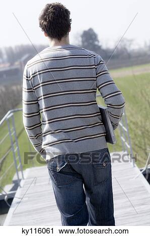 Man walking on terrace roof, holding laptop computer, rear view View Large Photo Image Stock Image - Man walking on terrace roof, holding laptop computer, rear view. Fotosearch