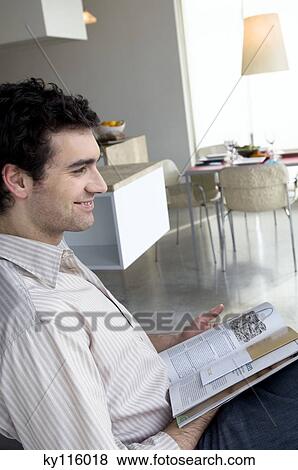 Smiling man reading in a living-room, side view View Large Photo Image Stock Photo - Smiling man reading in a living-room, side view. Fotosearch