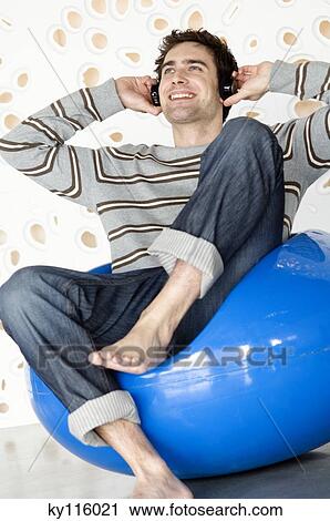 Smiling man wearing headphones, sitting in a blue armchair View Large Photo Image Stock Image - Smiling man wearing headphones, sitting in a blue armchair. Fotosearch