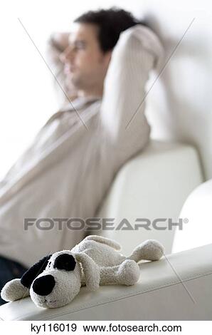 Stock Photo - Thinking man sitting on a sofa, stuffed dog in the foreground. Fotosearch