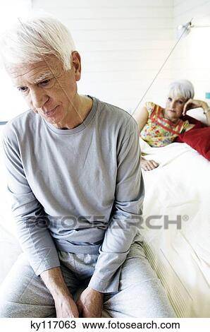 Sad looking senior man sitting on a bed, senior woman in background View Large Photo Image Stock Image - Sad looking senior man sitting on a bed, senior woman in background. Fotosearch