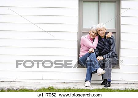 Stock Image - Senior couple embracing, sitting on a window sill. Fotosearch