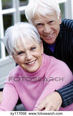 Stock Photograph - Senior couple embracing, smiling for the camera, outdoors. Fotosearch