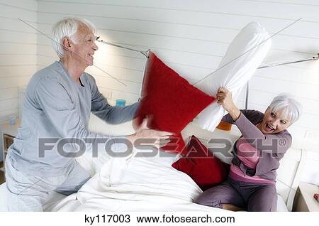 Senior couple having a pillow fight on a bed View Large Photo Image Stock Image - Senior couple having a pillow fight on a bed. Fotosearch