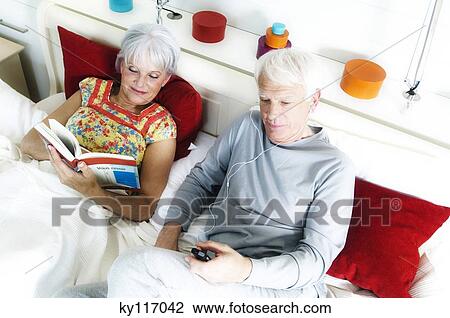 Senior couple in bed, woman reading, man listening to MP3 player, elevated view View Large Photo Image Stock Image - Senior couple in bed, woman reading, man listening to MP3 player, elevated view. Fotosearch