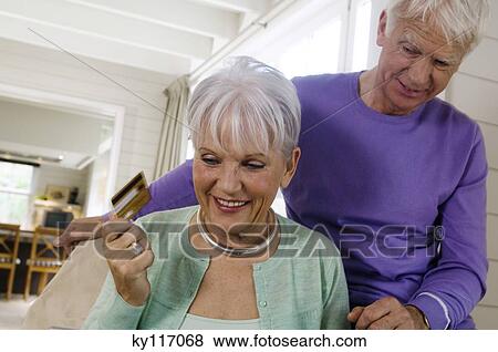 Senior couple inthe living-room, woman holding credit card View Large Photo Image Stock Photo - Senior couple inthe living-room, woman holding credit card. Fotosearch