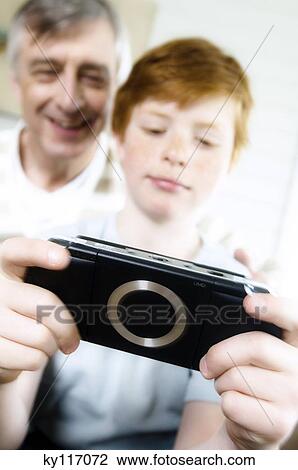 Stock Image - Senior man and boy playing Playstation Portable. Fotosearch