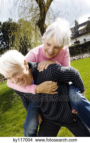 Picture - Senior man carrying senior woman on his back in garden. Fotosearch