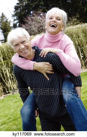 Stock Photo - Senior man carrying senior woman on his back in garden. Fotosearch