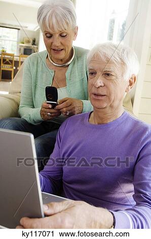 Stock Image - Senior man using laptop computer, senior woman using mobile phone. Fotosearch