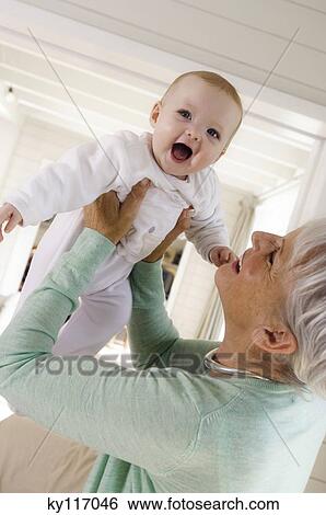 Stock Photograph - Senior woman lifting baby girl in the air. Fotosearch