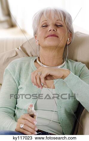 Stock Image - Senior woman listening to MP3 player, eyes shut. Fotosearch