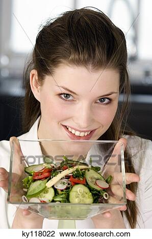 Stock Image - Portrait of a young smiling woman holding mixed salad. Fotosearch