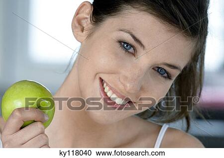 Stock Image - Portrait of a young smiling woman holding an apple. Fotosearch