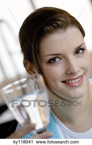 Stock Image - Portrait of a young smiling woman holding a glass of water. Fotosearch