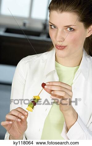 Portrait of a young woman eating a fruit skewer View Large Photo Image Picture - Portrait of a young woman eating a fruit skewer. Fotosearch