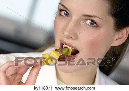 Portrait of a young woman eating a fruit skewer View Large Photo Image Stock Image - Portrait of a young woman eating a fruit skewer. Fotosearch