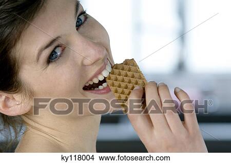 Picture - Portrait of a young woman eating a wafer. Fotosearch