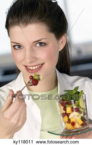 Stock Image - Portrait of a young woman eating fruit salad. Fotosearch