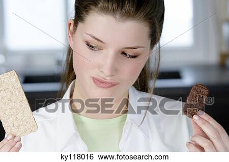 Portrait of a young woman hesitating between a chocolate biscuit and a diet biscuit View Large Photo Image Stock Photograph - Portrait of a young woman hesitating between a chocolate biscuit and a diet biscuit. Fotosearch