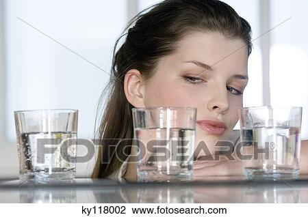 Portrait of a young woman looking at 3 glasses of water View Large Photo Image Stock Image - Portrait of a young woman looking at 3 glasses of water. Fotosearch