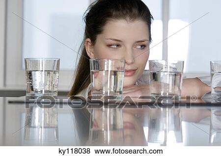 Portrait of a young woman looking at 4 glasses of water View Large Photo Image Stock Photo - Portrait of a young woman looking at 4 glasses of water. Fotosearch