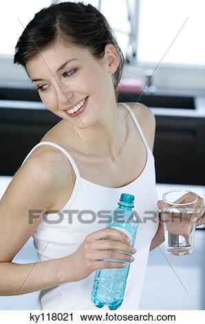Young smiling woman holding a glass and a bottle of mineral water View Large Photo Image Stock Image - Young smiling woman holding a glass and a bottle of mineral water. Fotosearch