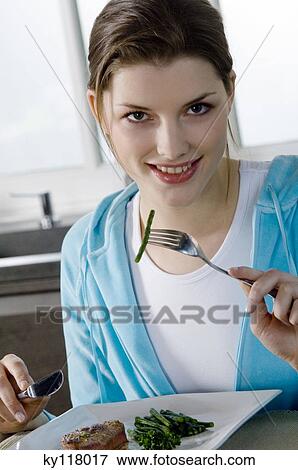 Stock Photo - Young woman eating meat and string beans. Fotosearch