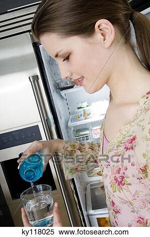 Stock Photography - Young woman in profile pouring water into a glass. Fotosearch