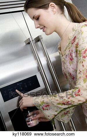 Young woman pouring water from a refrigerator water dispenser into a glass View Large Photo Image Stock Photo - Young woman pouring water from a refrigerator water dispenser into a glass. Fotosearch