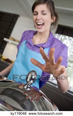 Woman in the kitchen, burning her fingers, trying to lift a pan lid View Large Photo Image Stock Photo - Woman in the kitchen, burning her fingers, trying to lift a pan lid. Fotosearch