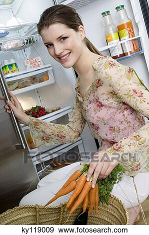 Young smiling woman filling refrigerator, holding carrots View Large Photo Image Stock Photo - Young smiling woman filling refrigerator, holding carrots. Fotosearch
